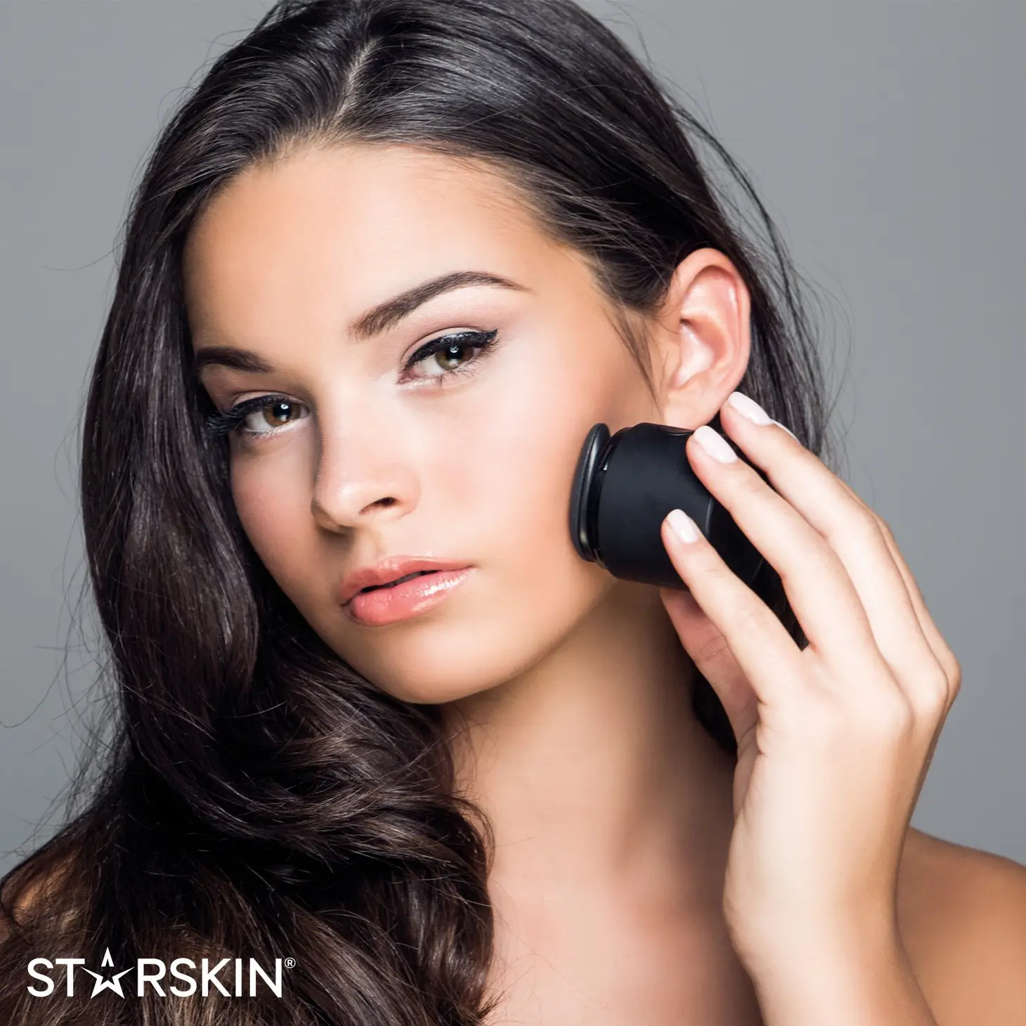 Frau verwendet ein schwarzes Schönheitsgerät auf ihrem Gesicht. Text: STARSKIN.