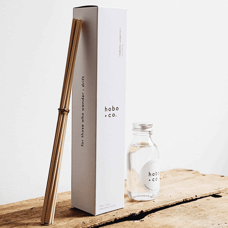hobo-co-raspberry-pepper-reed-diffuser_optimized Hobo+Co. Himbeer-Pfeffer-Diffusor mit Stäbchen und Flasche auf einem Holztisch.