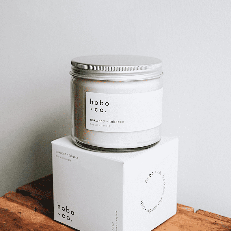 hobo-co-oakwood-tobacco-essential-oil-candle-250ml Hobo + Co. Oakwood & Tobacco Duftkerze in Glasbehälter auf weißer Box, 250 ml.